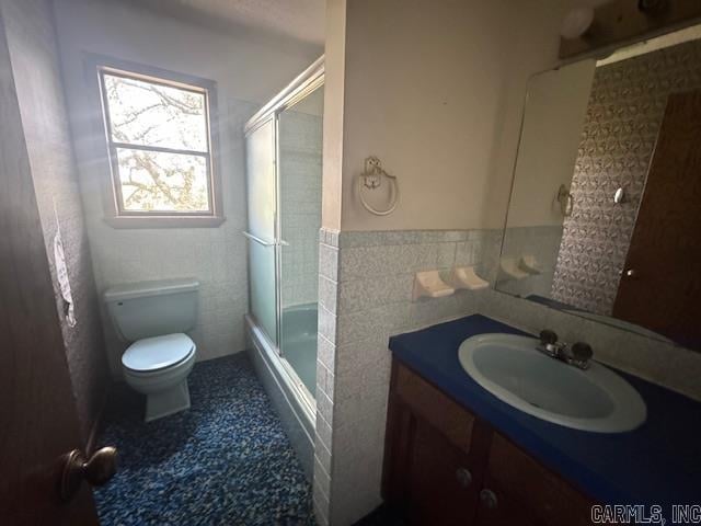 full bathroom featuring enclosed tub / shower combo, vanity, tile walls, and toilet