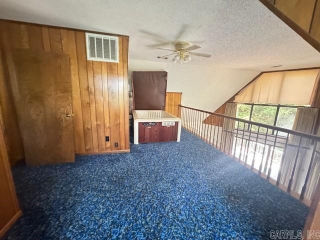 interior space with ceiling fan, wood walls, a textured ceiling, dark colored carpet, and vaulted ceiling