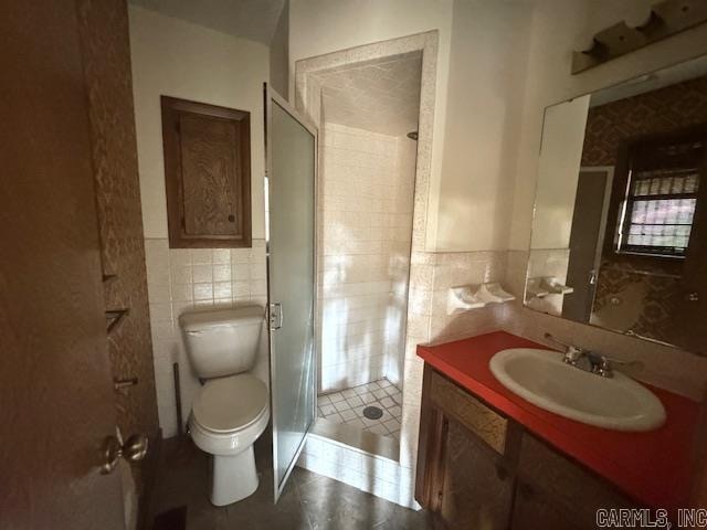 bathroom with tile walls, a shower with door, vanity, and toilet