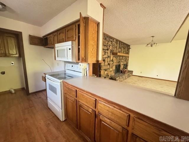 kitchen with white appliances, a stone fireplace, a textured ceiling, a notable chandelier, and dark hardwood / wood-style flooring