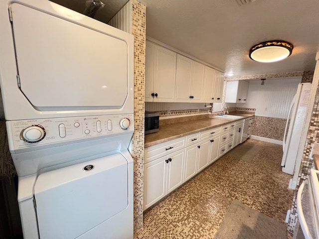 washroom with a textured ceiling, stacked washer / dryer, and sink