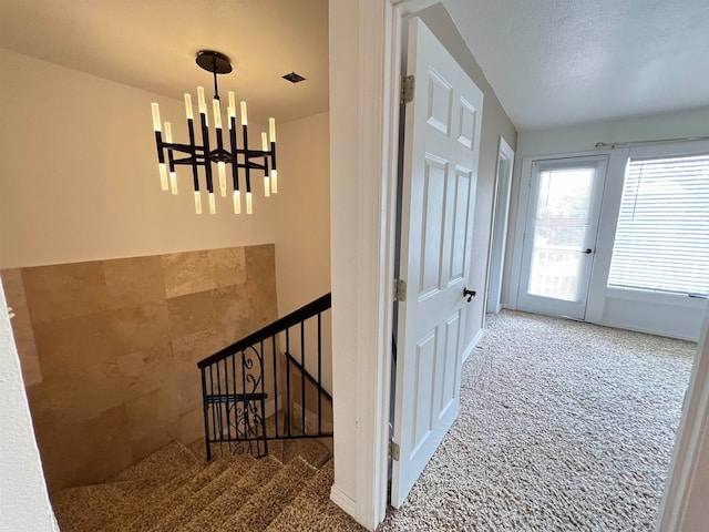 staircase featuring carpet floors, a textured ceiling, and a notable chandelier