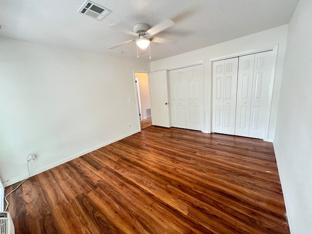 unfurnished bedroom featuring a textured ceiling, two closets, dark hardwood / wood-style floors, and ceiling fan