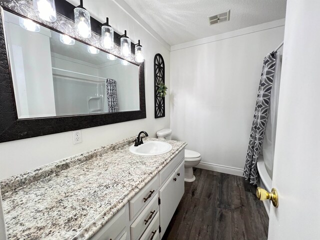 full bathroom with vanity, a textured ceiling, shower / bath combo with shower curtain, hardwood / wood-style flooring, and toilet