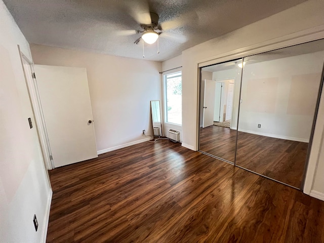 unfurnished bedroom with dark wood-type flooring, an AC wall unit, a closet, a textured ceiling, and ceiling fan