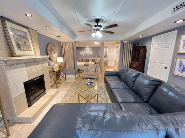 living room with a tiled fireplace, ceiling fan, and a tray ceiling