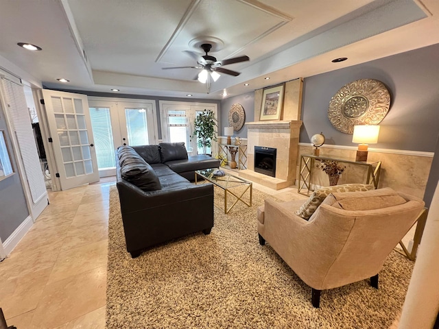 living room with a tray ceiling, ceiling fan, a tiled fireplace, and french doors