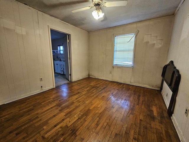 spare room with a textured ceiling, ceiling fan, dark hardwood / wood-style floors, and wood walls