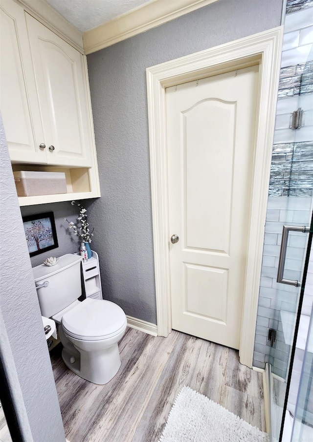 bathroom with a shower with shower door, a textured ceiling, wood-type flooring, crown molding, and toilet