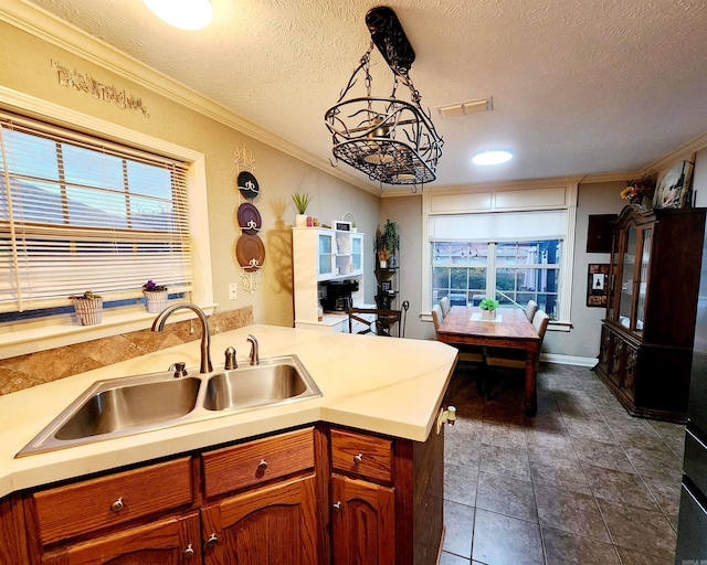 kitchen featuring kitchen peninsula, a textured ceiling, decorative light fixtures, ornamental molding, and sink