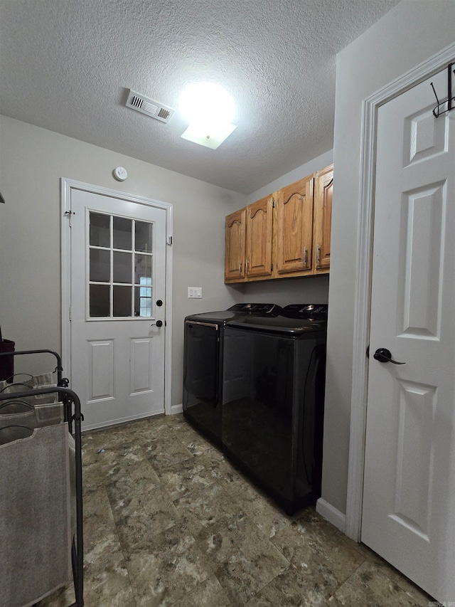 washroom with a textured ceiling, washer and clothes dryer, and cabinets