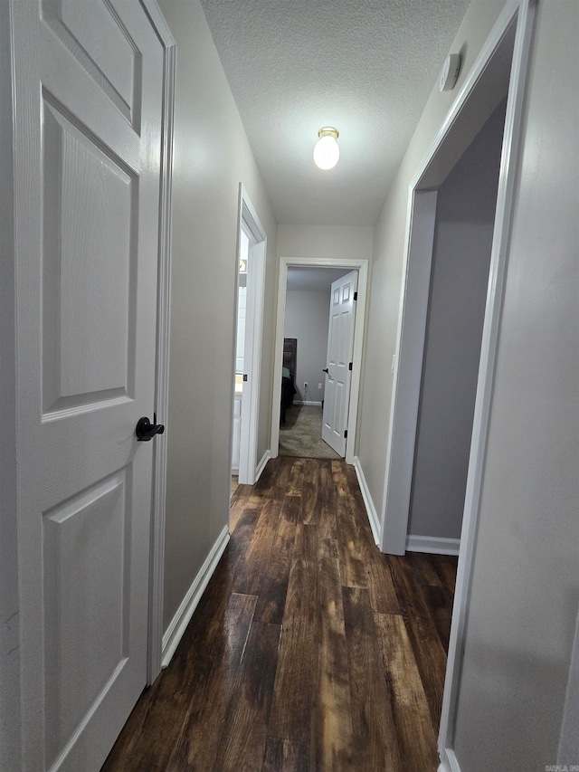 hall with a textured ceiling and dark wood-type flooring