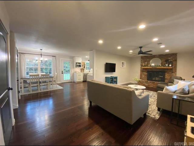 living room featuring ceiling fan with notable chandelier, a fireplace, and dark wood-type flooring