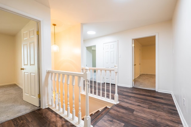 hallway featuring baseboards, dark wood-type flooring, and an upstairs landing