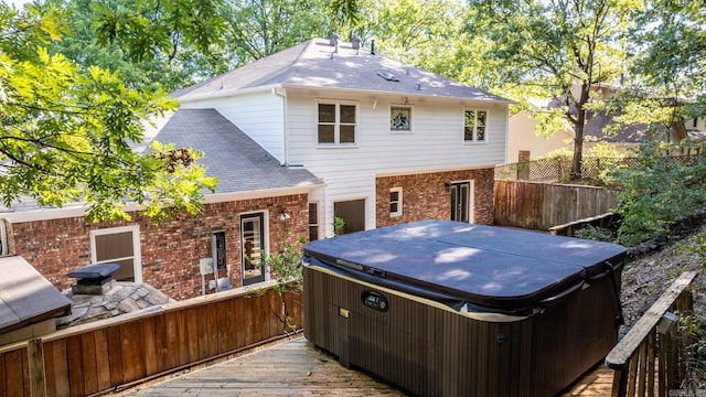 back of property with brick siding, a shingled roof, a hot tub, fence, and a wooden deck