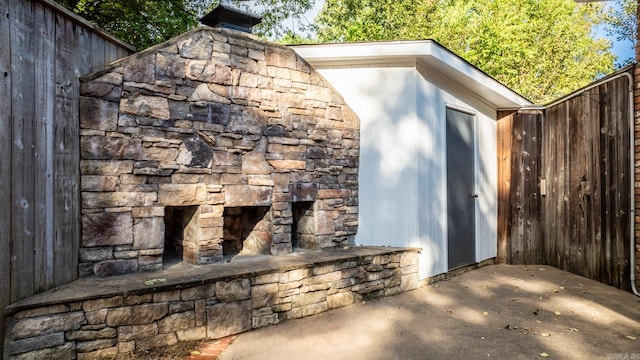 view of outdoor structure featuring an outdoor stone fireplace and fence