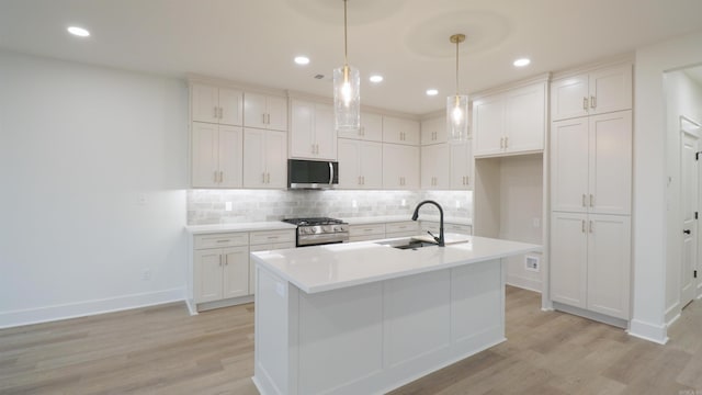 kitchen featuring appliances with stainless steel finishes, sink, decorative light fixtures, light hardwood / wood-style floors, and white cabinetry