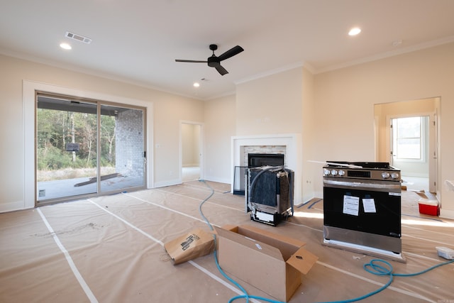 living room featuring ceiling fan, a wealth of natural light, a stone fireplace, and crown molding