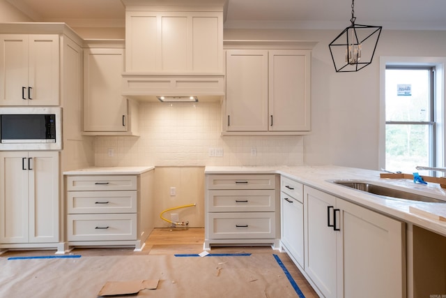 kitchen featuring sink, an inviting chandelier, stainless steel microwave, white cabinets, and pendant lighting