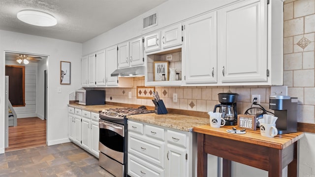 kitchen with a textured ceiling, backsplash, stainless steel stove, and white cabinets