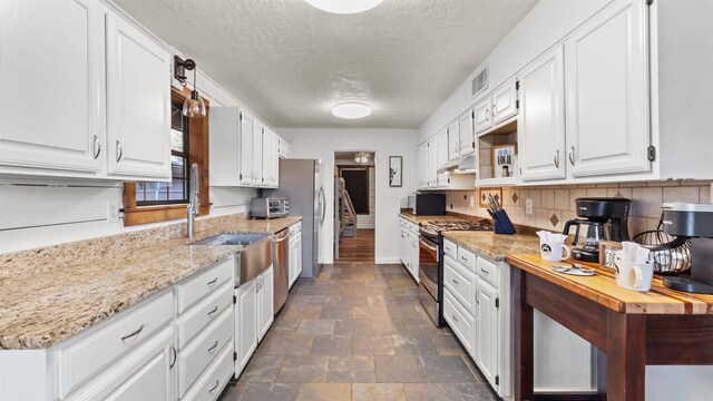 kitchen with appliances with stainless steel finishes, decorative backsplash, white cabinetry, light stone counters, and a textured ceiling