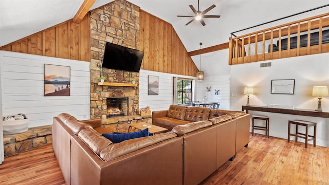 living room with light hardwood / wood-style floors, wood walls, high vaulted ceiling, a stone fireplace, and ceiling fan