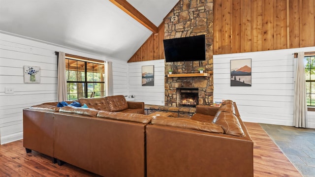 living room with a stone fireplace, wooden walls, high vaulted ceiling, and plenty of natural light