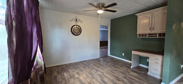 unfurnished office featuring dark wood-type flooring, built in desk, and ceiling fan