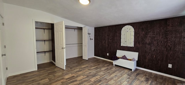 unfurnished bedroom with vaulted ceiling, dark hardwood / wood-style floors, and wooden walls