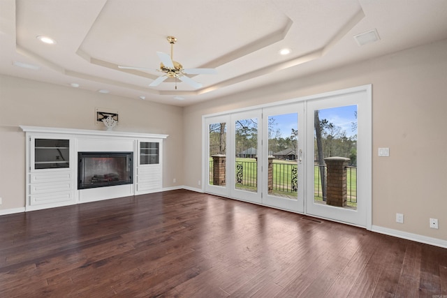 unfurnished living room featuring a raised ceiling, ceiling fan, and dark wood-type flooring