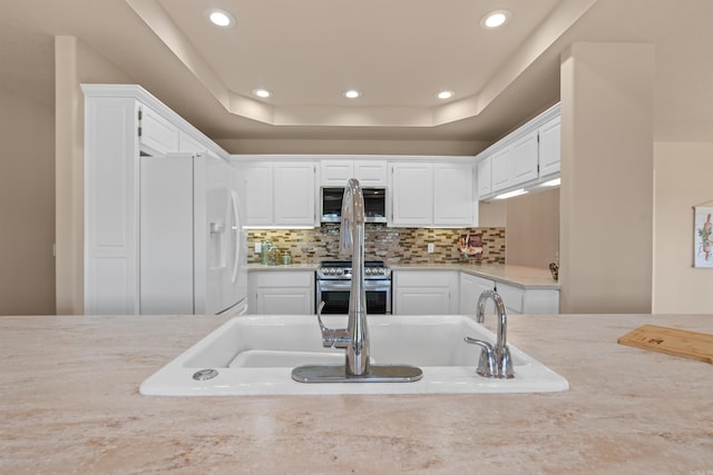 kitchen with appliances with stainless steel finishes, decorative backsplash, a tray ceiling, and white cabinets