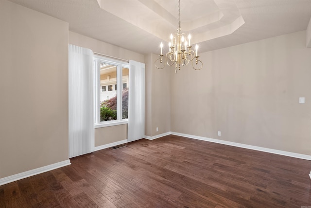 empty room featuring a raised ceiling, an inviting chandelier, and dark wood-type flooring