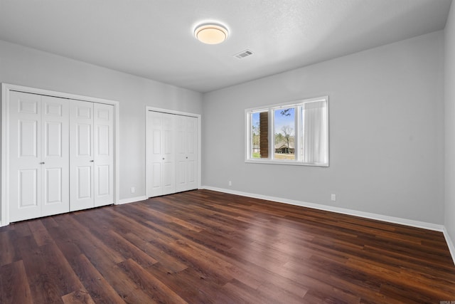 unfurnished bedroom featuring two closets and dark wood-type flooring