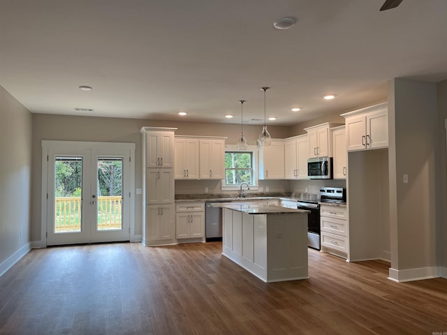 kitchen with white cabinets, a center island, appliances with stainless steel finishes, and hardwood / wood-style flooring