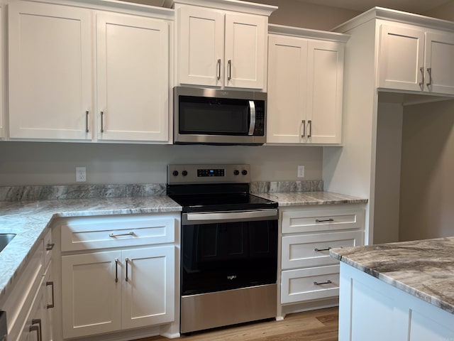 kitchen with light stone countertops, white cabinets, light hardwood / wood-style floors, and appliances with stainless steel finishes