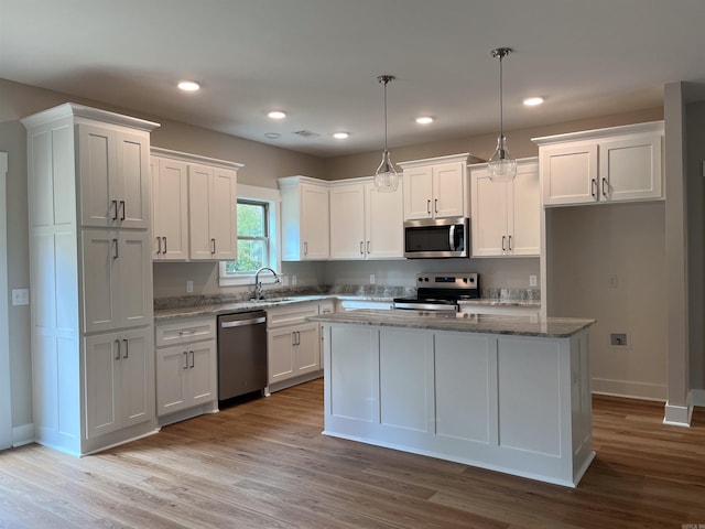 kitchen with hanging light fixtures, sink, a kitchen island, white cabinetry, and stainless steel appliances