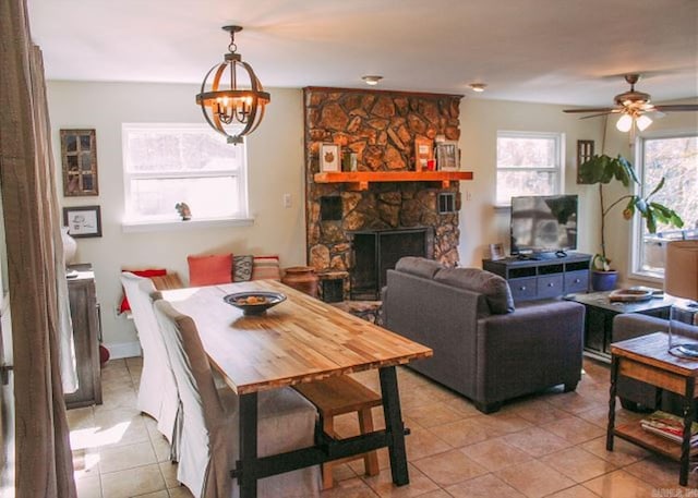 tiled dining area featuring ceiling fan with notable chandelier and a fireplace