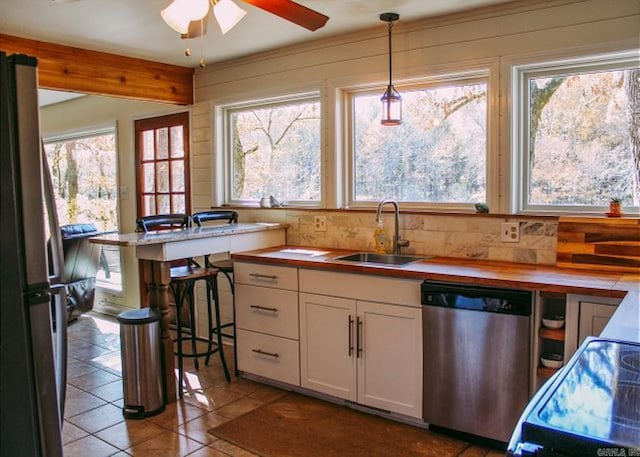 kitchen featuring ceiling fan, sink, wooden counters, decorative light fixtures, and stainless steel appliances