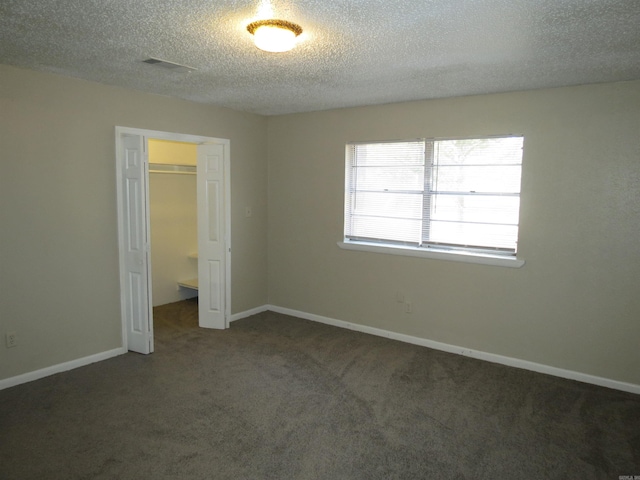 unfurnished bedroom featuring a textured ceiling, a spacious closet, dark carpet, and a closet