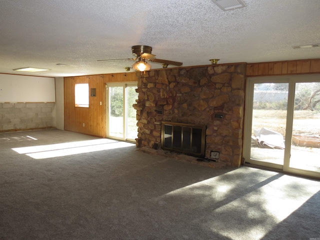 unfurnished living room with ceiling fan, a textured ceiling, wooden walls, carpet, and a fireplace