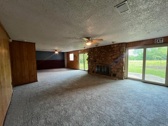 unfurnished living room featuring ceiling fan, a fireplace, wood walls, and a healthy amount of sunlight