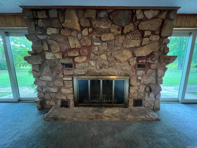 interior details featuring a stone fireplace, a textured ceiling, wood walls, and carpet