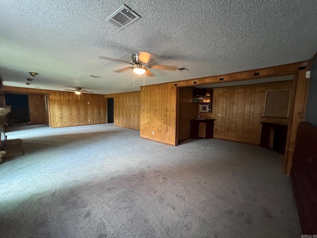 unfurnished living room with wooden walls, ceiling fan, and light colored carpet