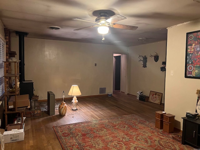 interior space with dark wood-type flooring, ceiling fan, and a wood stove