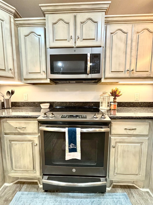 kitchen with stainless steel appliances, dark stone countertops, and light wood-type flooring