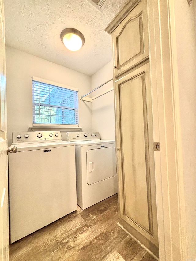 clothes washing area with wood-type flooring, cabinets, washer and dryer, and a textured ceiling