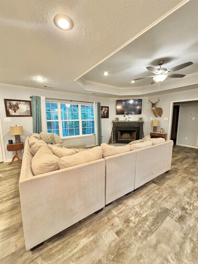 living room with a tray ceiling, ceiling fan, hardwood / wood-style flooring, and a textured ceiling