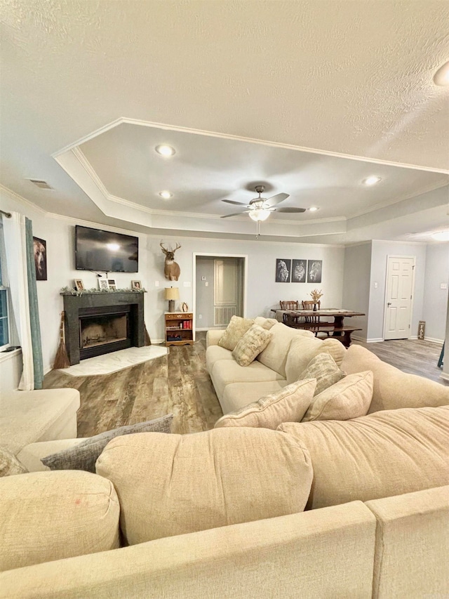 living room with a textured ceiling, a tray ceiling, hardwood / wood-style floors, and ceiling fan