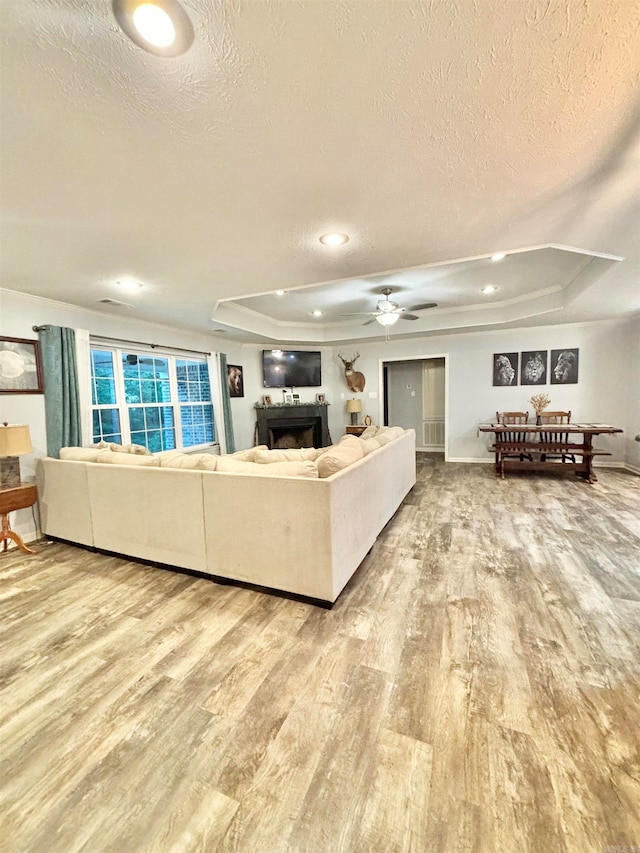 living room featuring wood-type flooring, a textured ceiling, a raised ceiling, and ceiling fan