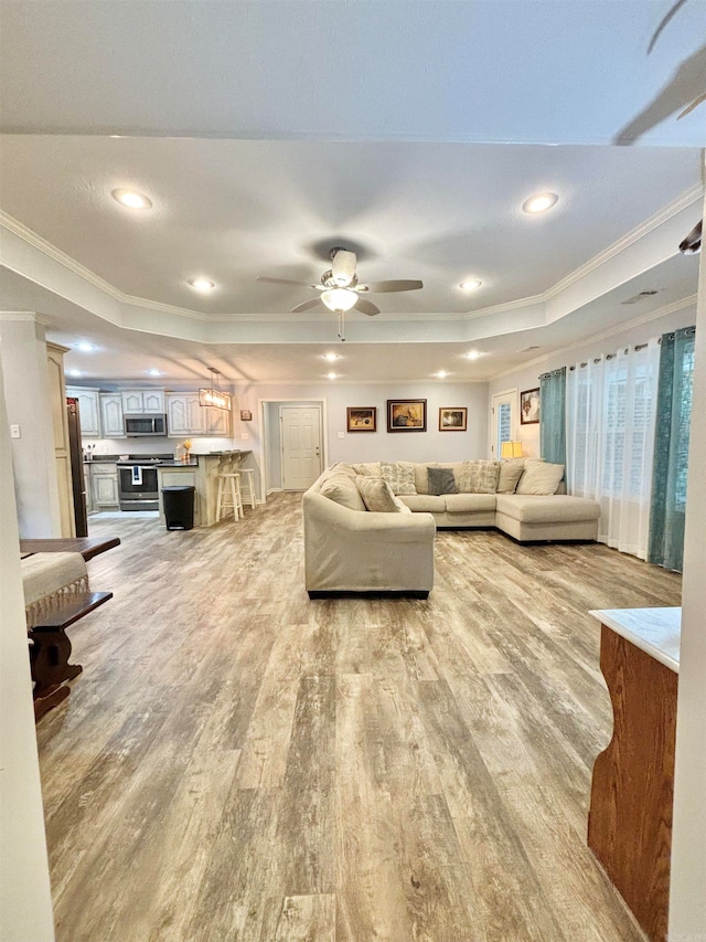 living room with ceiling fan, light wood-type flooring, ornamental molding, and a tray ceiling